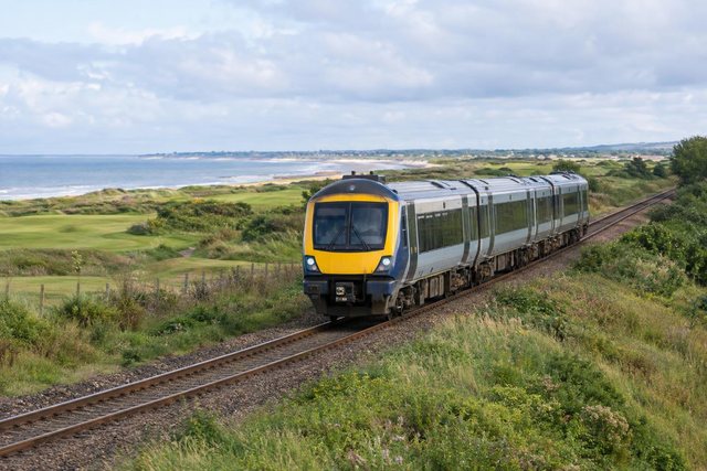 A passenger train travels along coastal tracks through green countryside beside the sea in Angus.